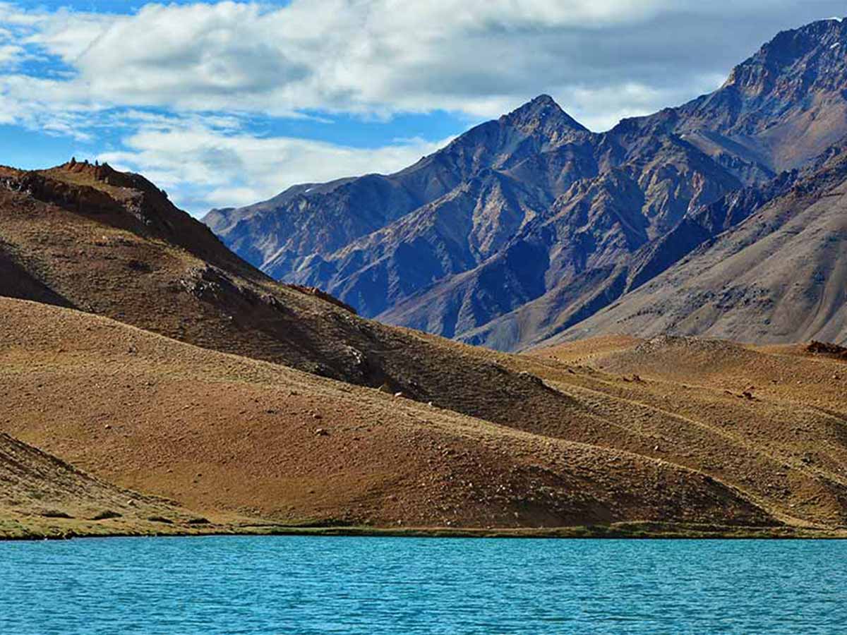 Chandratal lake surrounded by mountains on bright cloudy day