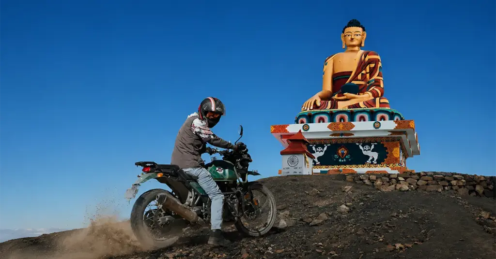A motorcyclist drifting past the giant golden Buddha statue at Langza village on an adventurous Spiti bike trip.