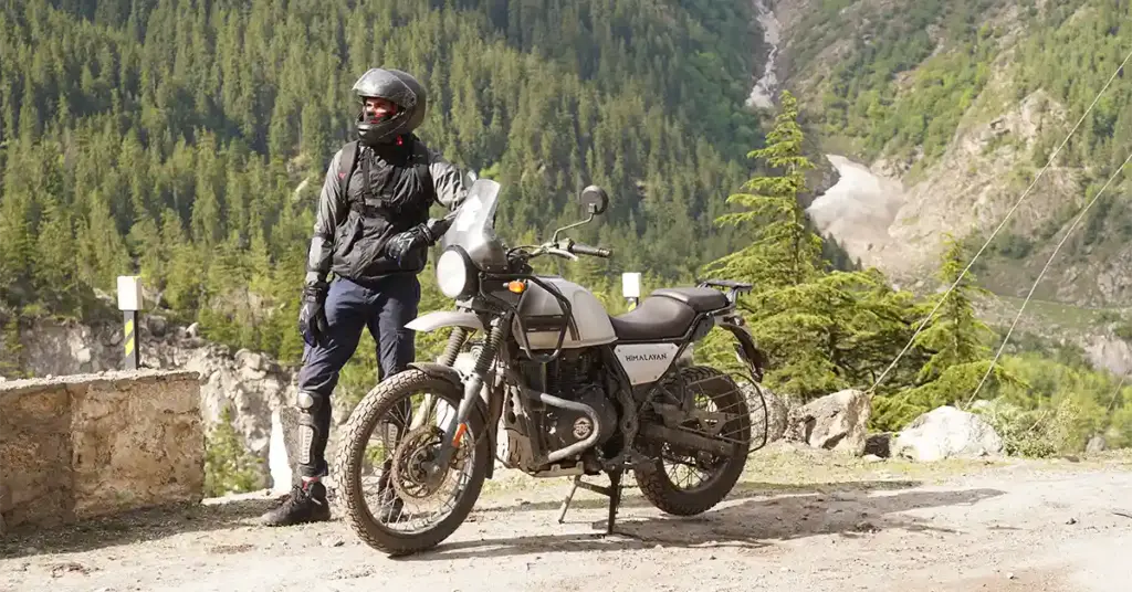 Rider with Royal Enfield Himalayan on a rough Spiti mountain road surrounded by dense pine forest on the Manali-Kaza approach