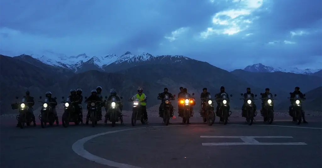 Motorcyclists parked on a helipad at dusk against snow-capped peaks in Nako Village during a Spiti bike trip.