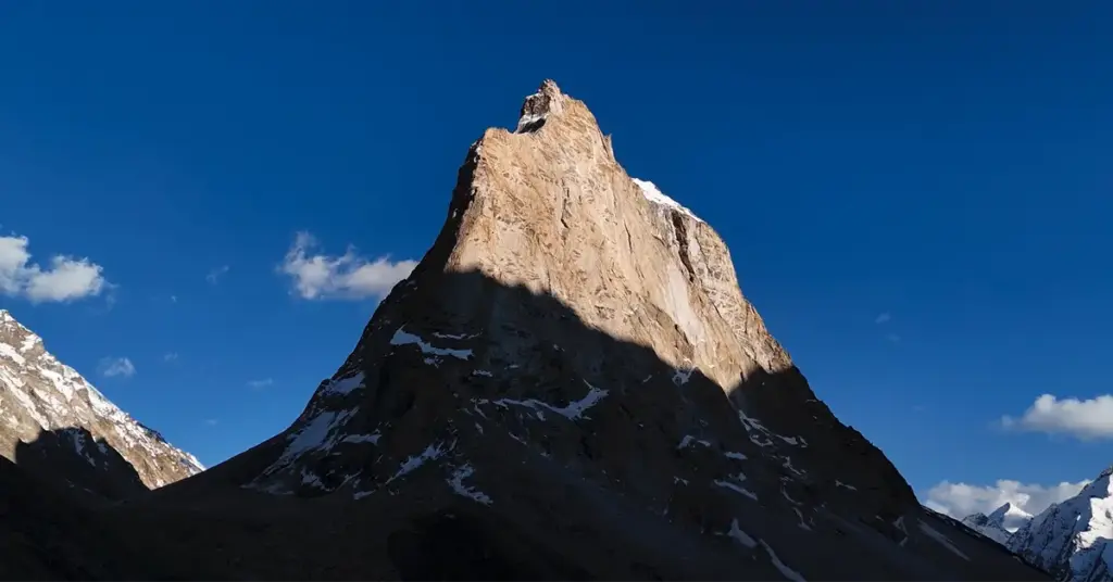 The sacred, standalone rocky peak of Gonbo Rangjon mountain towering into a deep blue sky, a famous natural landmark and campsite along the Shinku La route to Zanskar Valley.
