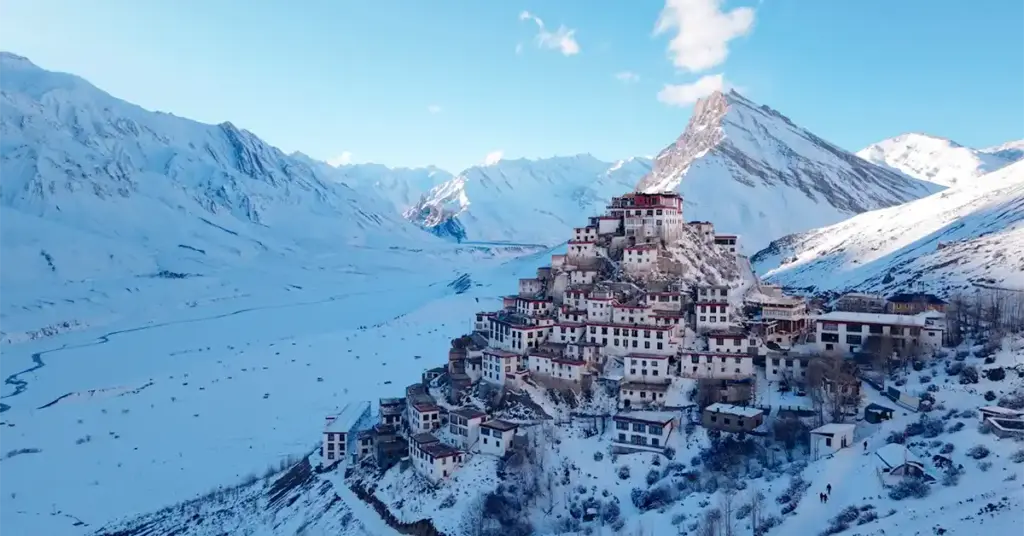 A striking high-angle view of the iconic Key Monastery perched on a hill, completely enveloped by a massive, snow-covered landscape and frozen mountain valley in winter.