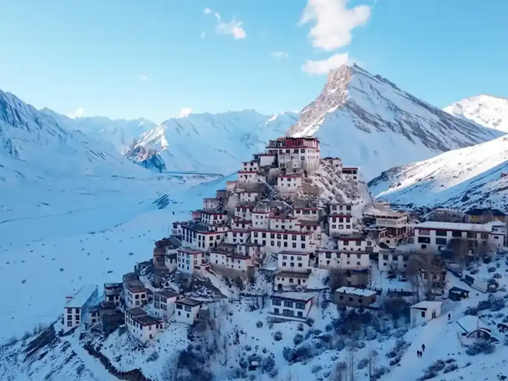 A striking high-angle view of the iconic Key Monastery perched on a hill, completely enveloped by a massive, snow-covered landscape and frozen mountain valley in winter.
