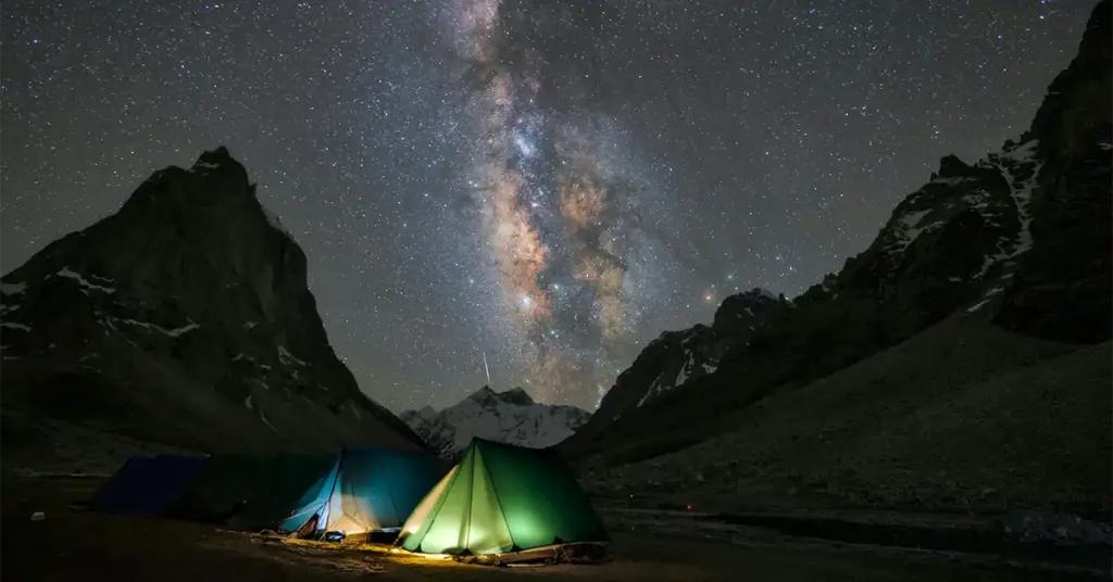 Astrophotography and stargazing at a high-altitude campsite near Gonbo Rangjon mountain peak in Zanskar Valley, Ladakh, featuring glowing green camping tents under a vibrant Milky Way galaxy night sky.