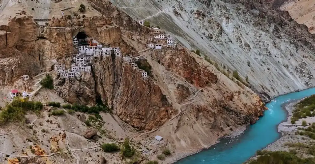High-angle view of the remote Phugtal Monastery (Phuktal Gompa) built entirely into a sheer cliff cave complex overlooking the brilliant turquoise Tsarap River in Zanskar, Ladakh.