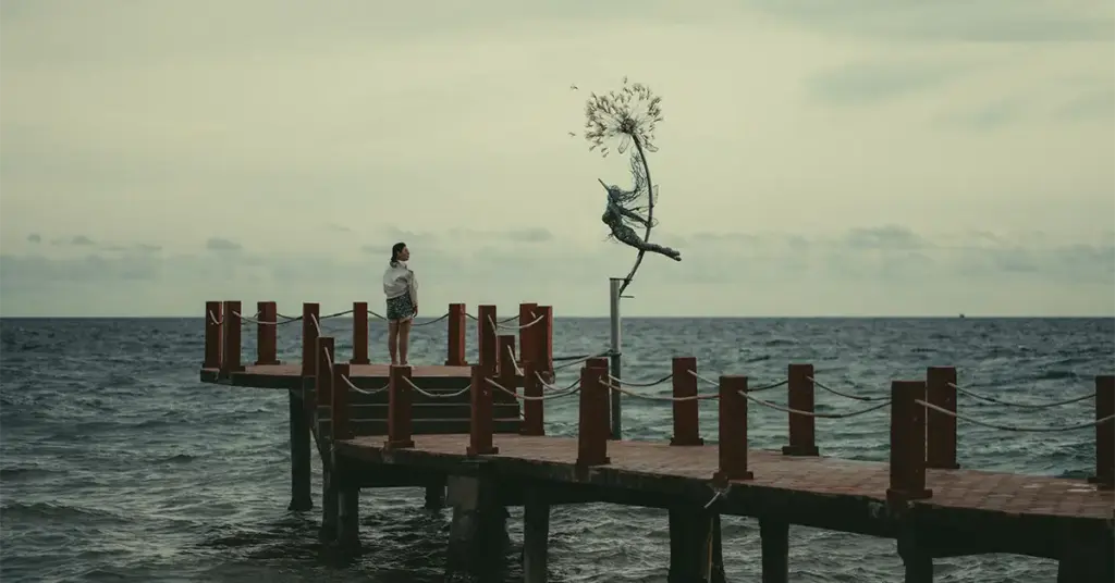 Overcast sky over a wooden pier with a wire fairy sculpture at Grand World Phu Quoc