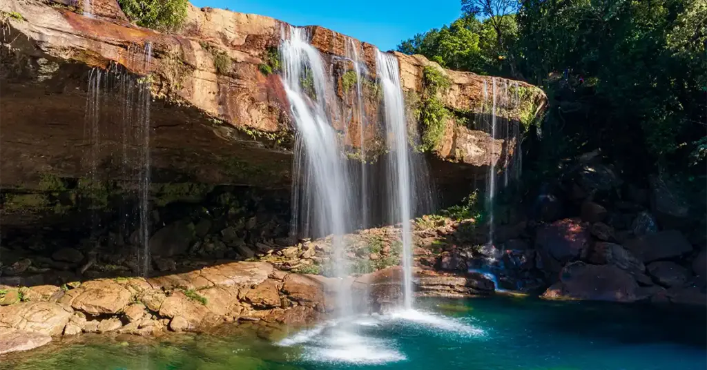 Krang Suri Falls cascading over red rocks into a turquoise pool in Jaintia Hills, Meghalaya