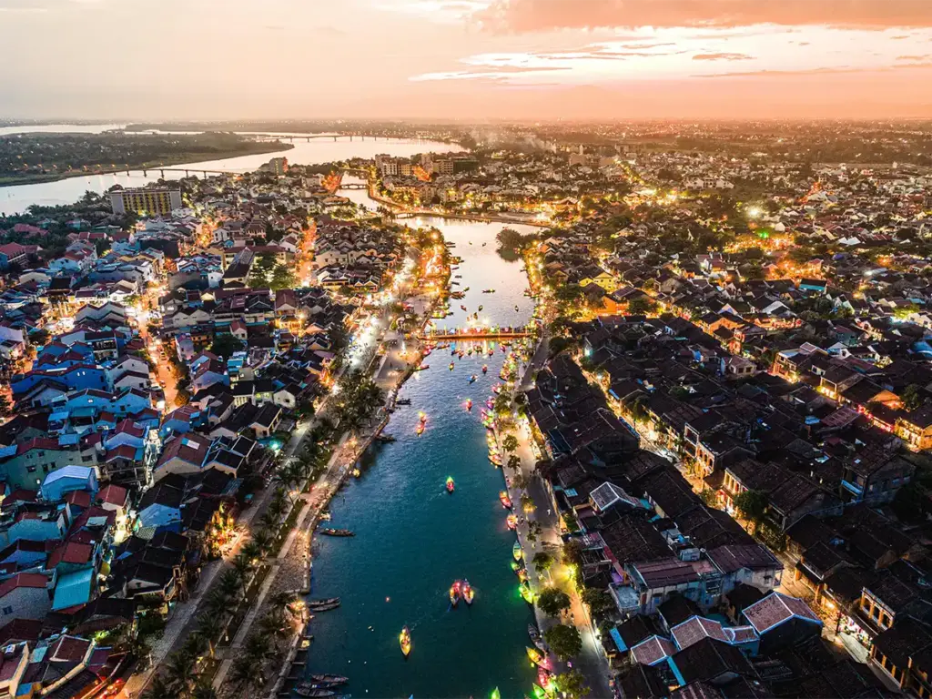 Hoi An at dusk — the Thu Bon River cuts through the old town as lantern boats and street lights switch on for the night.